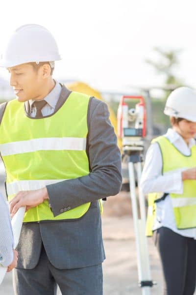 Land surveyors in safety vests and helmets reviewing plans on a construction site during an ALTA land title survey.
