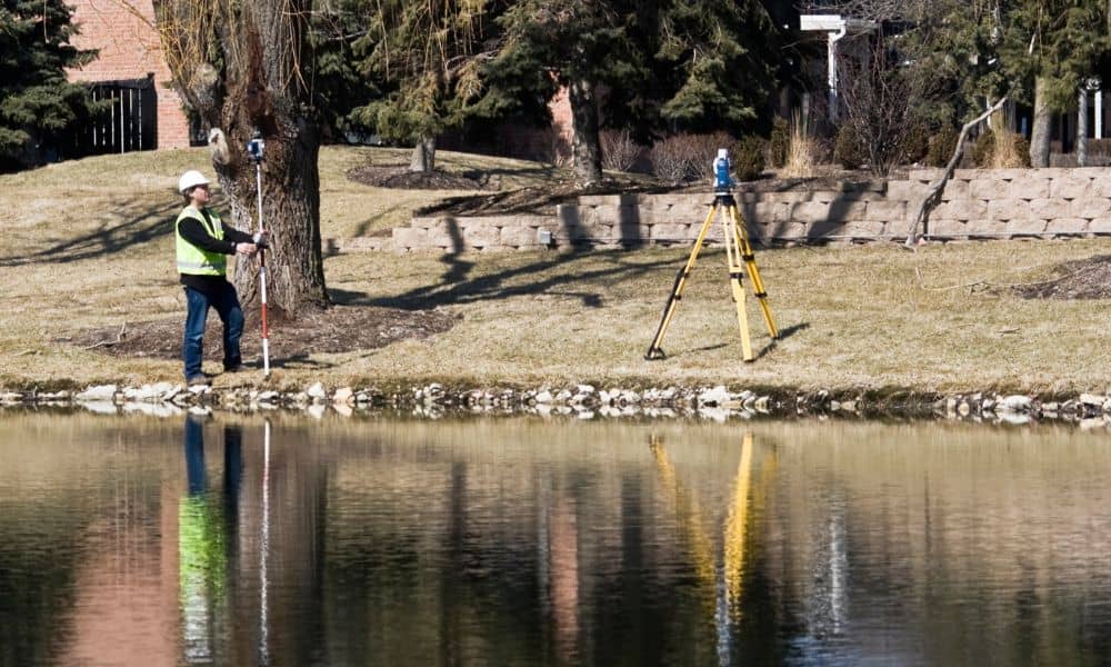 Land surveyor taking elevation measurements near the water, helping determine details needed for a FEMA elevation certificate
