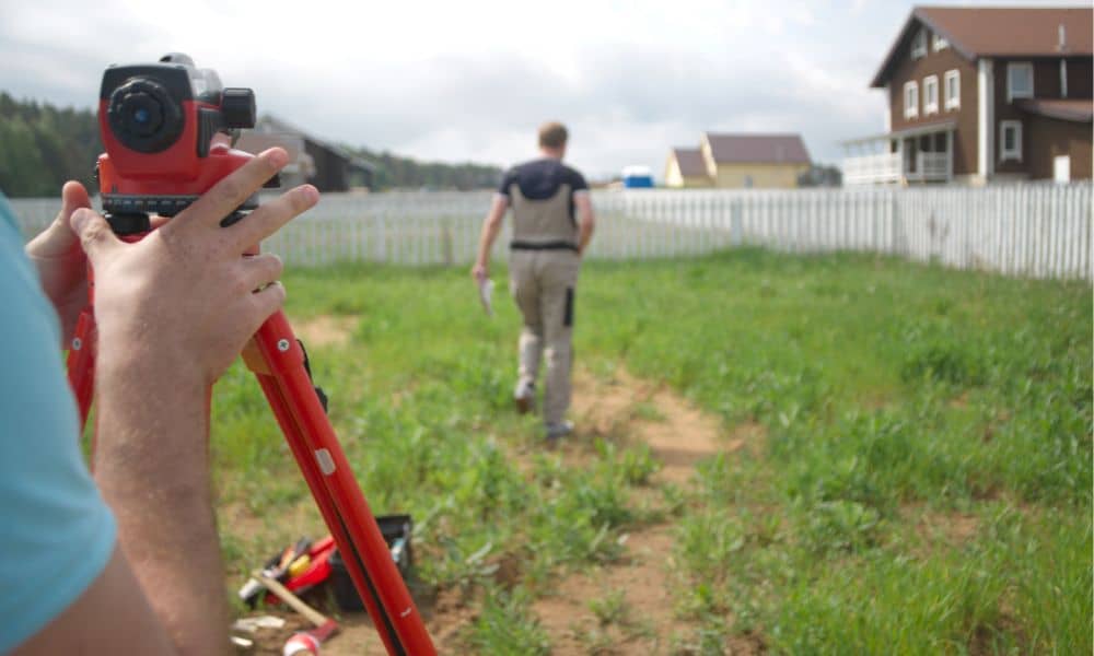 Surveyor conducting a residential boundary survey in a backyard to measure accurate property lines near a fence and house.