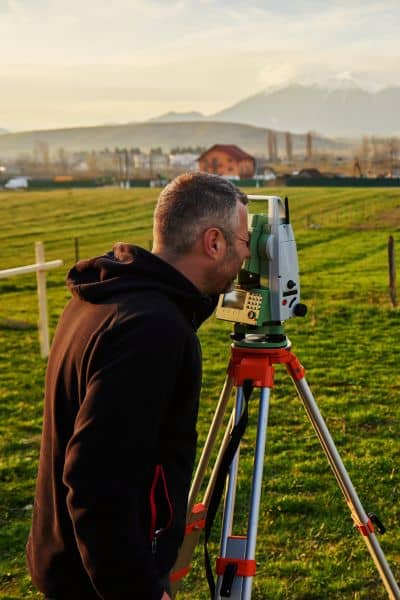 Surveyor using total station equipment to perform a property line survey near residential houses
