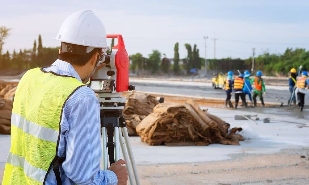 Licensed land surveyors using total station equipment to measure elevations and guide drainage construction work at a project site