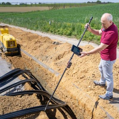 A construction surveyor checking measurements near active utility work on a construction site