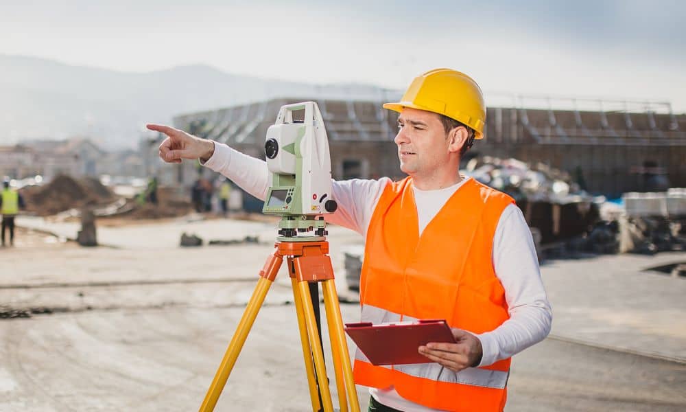 A licensed land surveyor using total station equipment to collect measurements on an active construction site before building begins