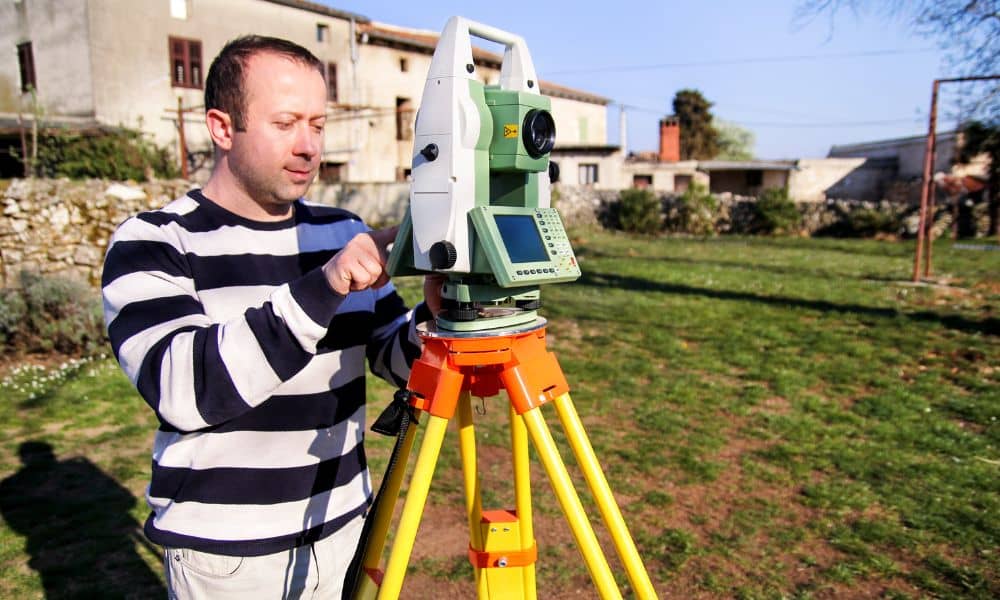 Professional land surveyor measuring a residential property boundary with a total station