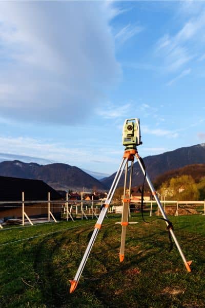 Professional land surveyor using a total station to locate property line markers on a residential lot